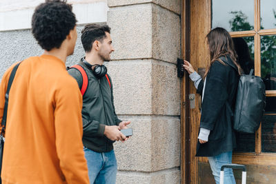 Young woman using combination lock at entrance while standing with friends