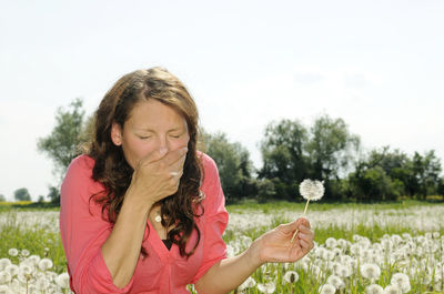 Woman holding a flowering plant against sky