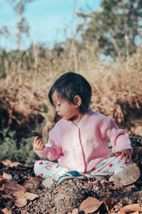 Cute baby girl looking at stone while sitting on land
