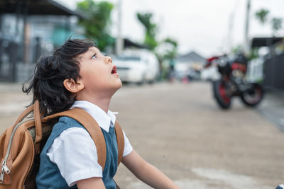 Side view of schoolboy looking up on street in city