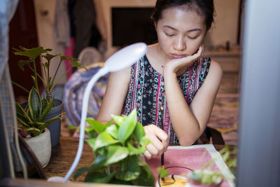 Woman looking away while sitting on potted plant at home