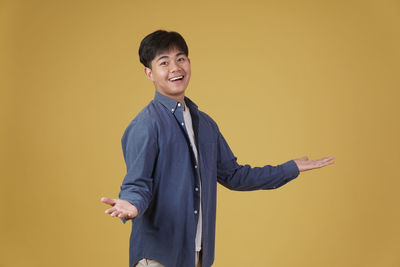 Portrait of young man standing against yellow background