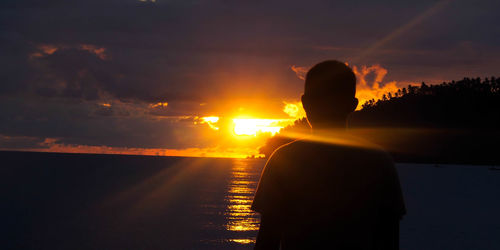 Silhouette man standing by sea against sunset sky