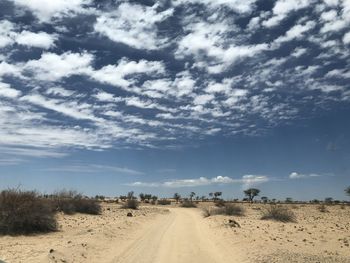 Dirt road amidst desert against sky