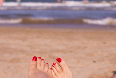 Low section of woman with red nail polish at beach