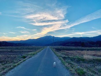 Empty road leading towards mountains against sky