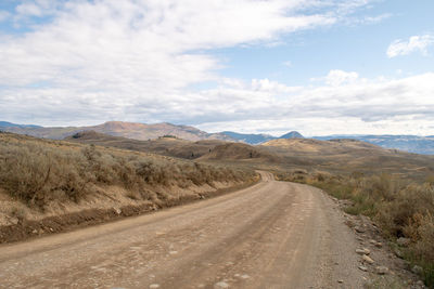 Dirt road amidst landscape against sky