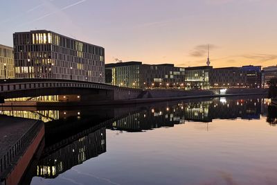 Bridge over river by buildings against sky at night