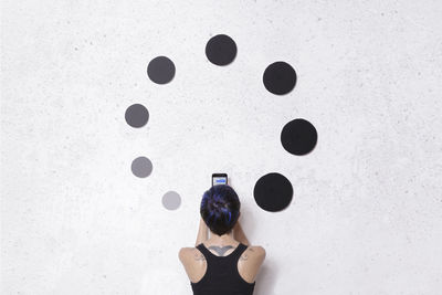 Rear view of woman with umbrella standing against white wall