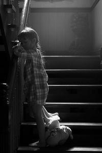 Girl holding stuffed toy standing by railing on staircase