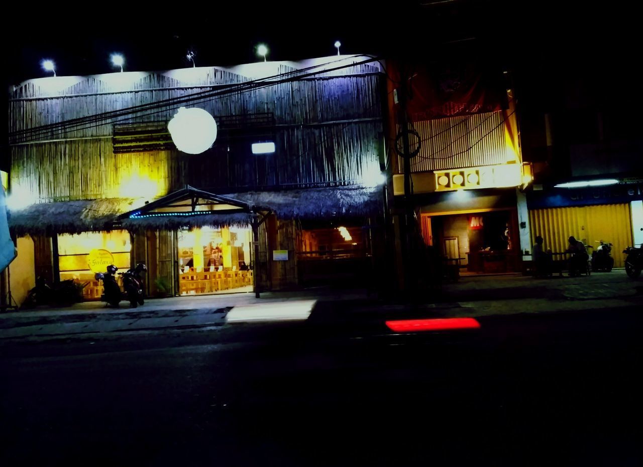 ILLUMINATED ROAD BY BUILDINGS AT NIGHT