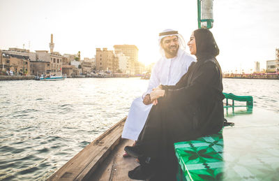 Cheerful couple talking while sitting in boat on river in city