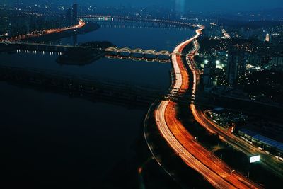 High angle view of light trails and illuminated bridge over river at night