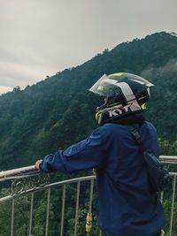 Man standing by railing on mountain against sky