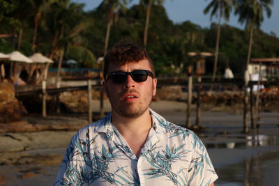 Portrait of young man wearing sunglasses standing at beach