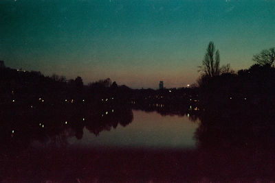 Reflection of silhouette trees in lake against sky at dusk