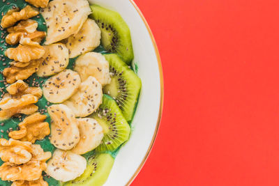 A spirulina smoothie bowl with banana, walnuts, kiwi and chia seeds on red background