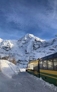 Snow covered train by mountain against sky