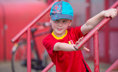 Boy wearing cap while holding red railing on footpath