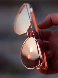 Close-up of hand holding sunglasses during sunset