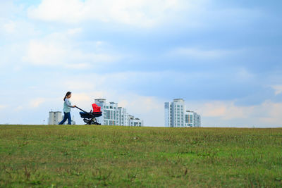 Woman with baby stroller walking on field against sky