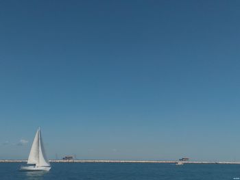 Sailboat sailing in sea against clear blue sky