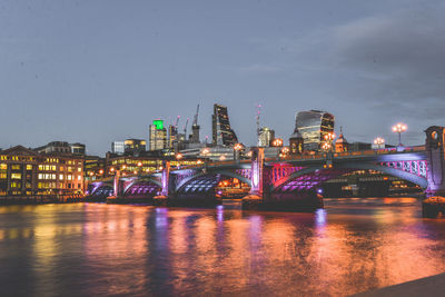 Illuminated bridge over river in city against sky at night