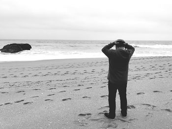 Rear view of depressed man standing with head in hand at beach