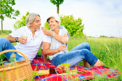 Happy friends sitting on basket at field against sky