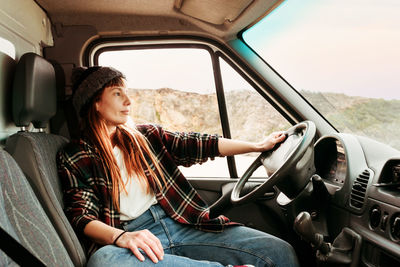 Traveling female hipster sitting in driver seat in parked truck in highlands