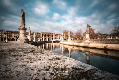 Statue of bridge over river against cloudy sky