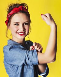 Portrait of smiling teenage girl flexing muscle against yellow background