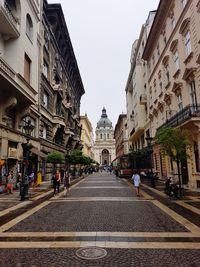 People walking on road amidst buildings in city against sky