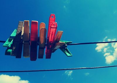 Low angle view of colorful clothespins on clothesline against blue sky