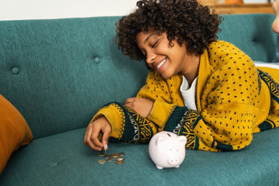 Young woman holding piggy bank on sofa at home