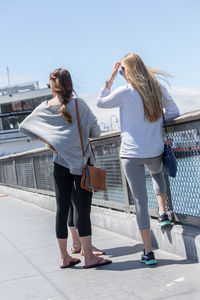 Rear view of women standing on railing against sky