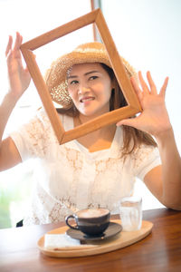 Portrait of a smiling young woman with drink on table