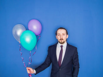Portrait of businessman holding balloons against blue background