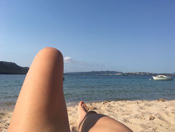 Low section of woman on beach against clear blue sky