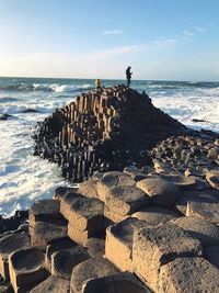 Distant view of men standing on groyne against sky