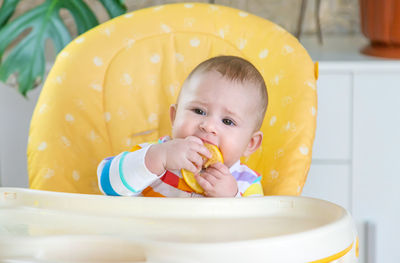 Cute baby girl eating orange fruit at home