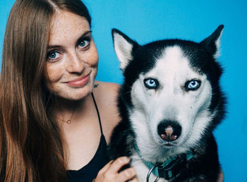 Close-up portrait of woman with siberian husky against blue background