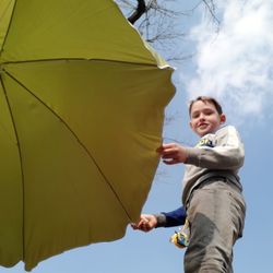 Low angle view of boy holding umbrella against sky