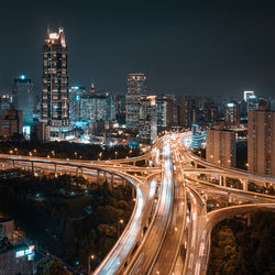 Light trails on road amidst illuminated buildings against sky at night