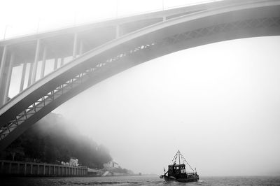 Arrabida bridge below trawler sailing on douro river in foggy weather