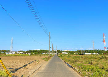 Road by electricity pylons against clear blue sky