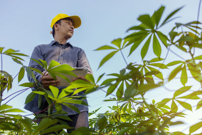 Young man looking away while standing on plant against sky