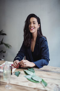 Portrait of smiling mid adult female entrepreneur sitting at table against wall in perfume workshop