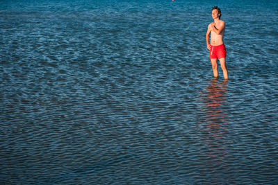 Shirtless man wearing red shorts standing in rippled sea
