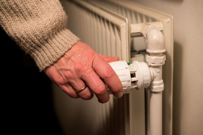 Female hand turning thermostatic valve on radiator